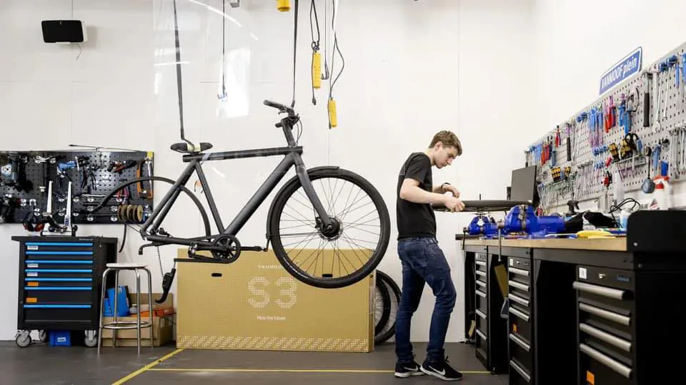 Werkplaats met een VanMoof S3 in de fietsstandaard en een monteur aan de werkbank